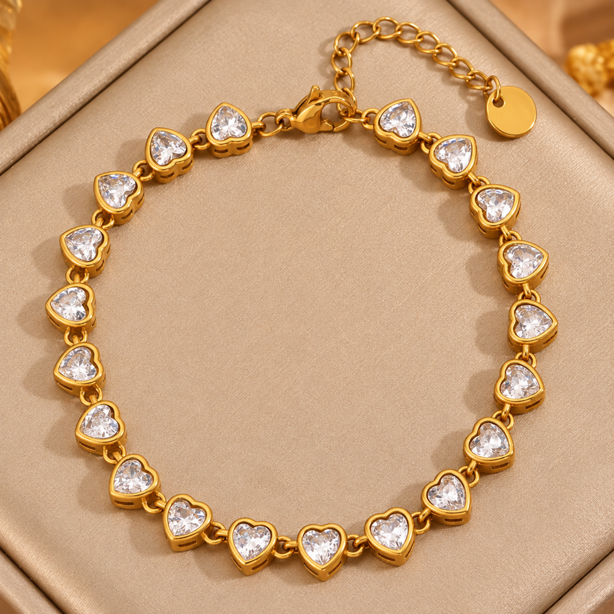 A gold heart-link bracelet with clear heart-shaped crystals, displayed on a beige jewelry box.