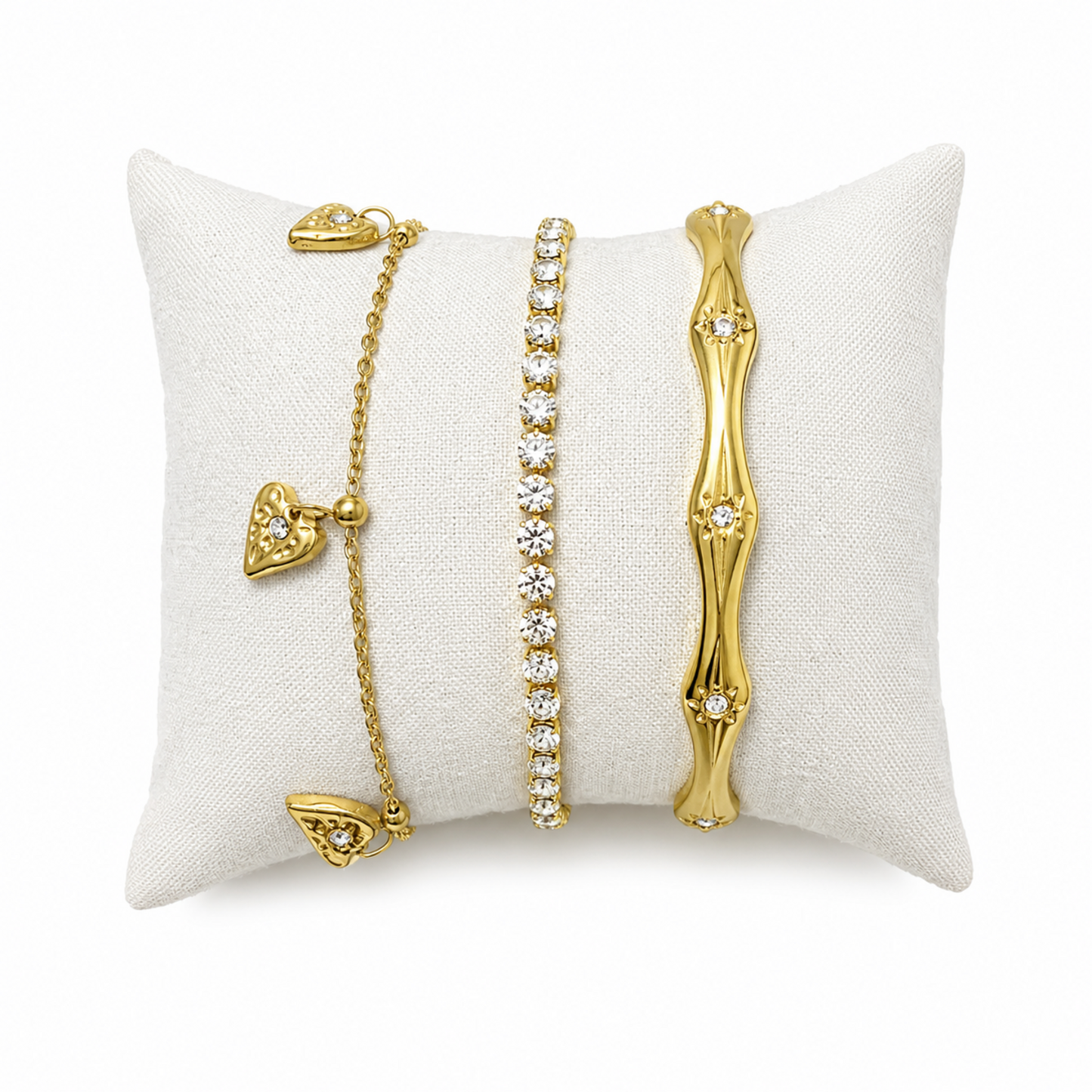 A three-piece gold-plated bracelet stack for women featuring an engraved wavy starburst bangle, a classic crystal tennis bracelet, and a fine link chain with three dangling gold heart charms