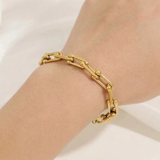 Gold chain bracelet on a wrist against a white background