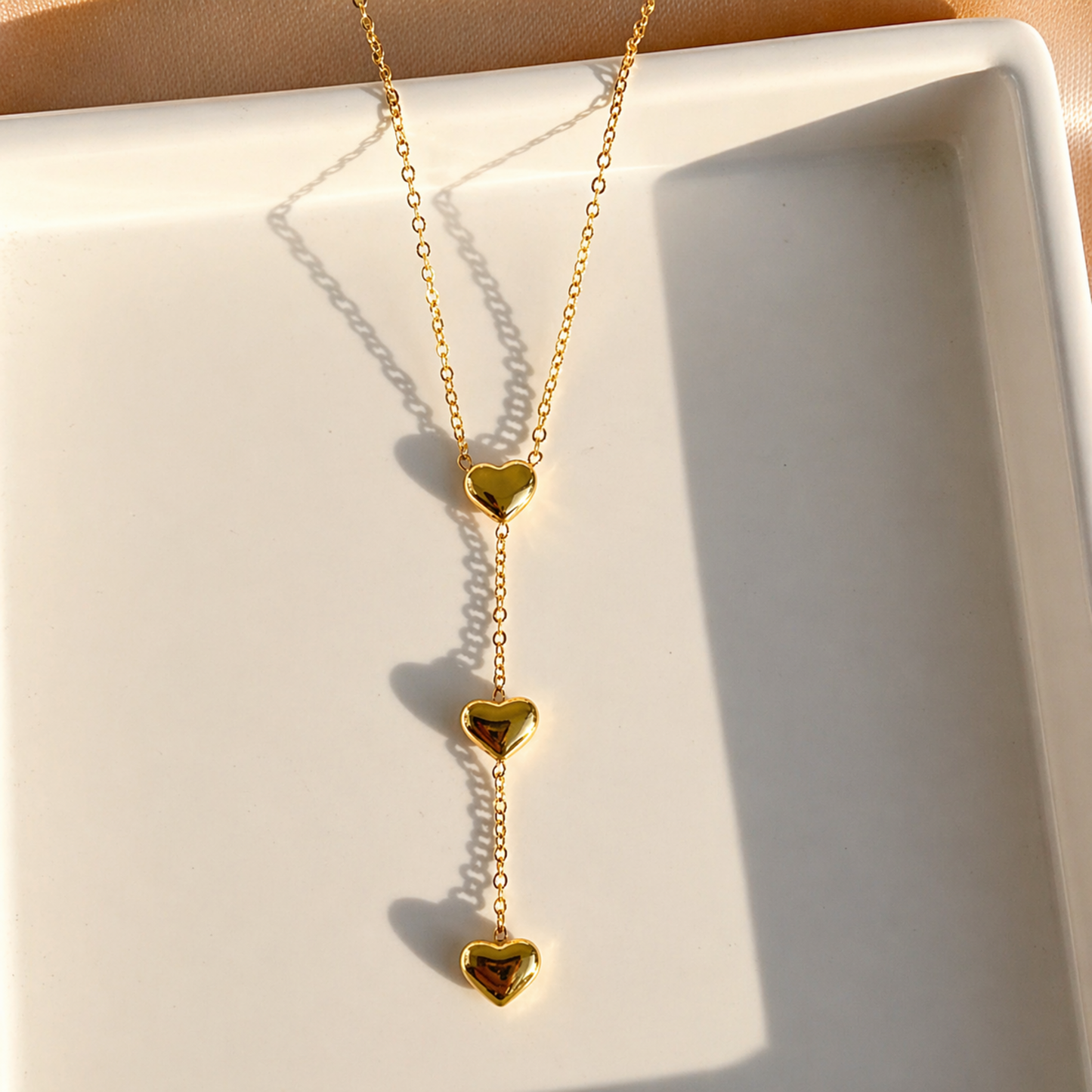 A close-view of a gold-plated stainless steel chain for women featuring a cascading vertical drop of three polished heart pendants