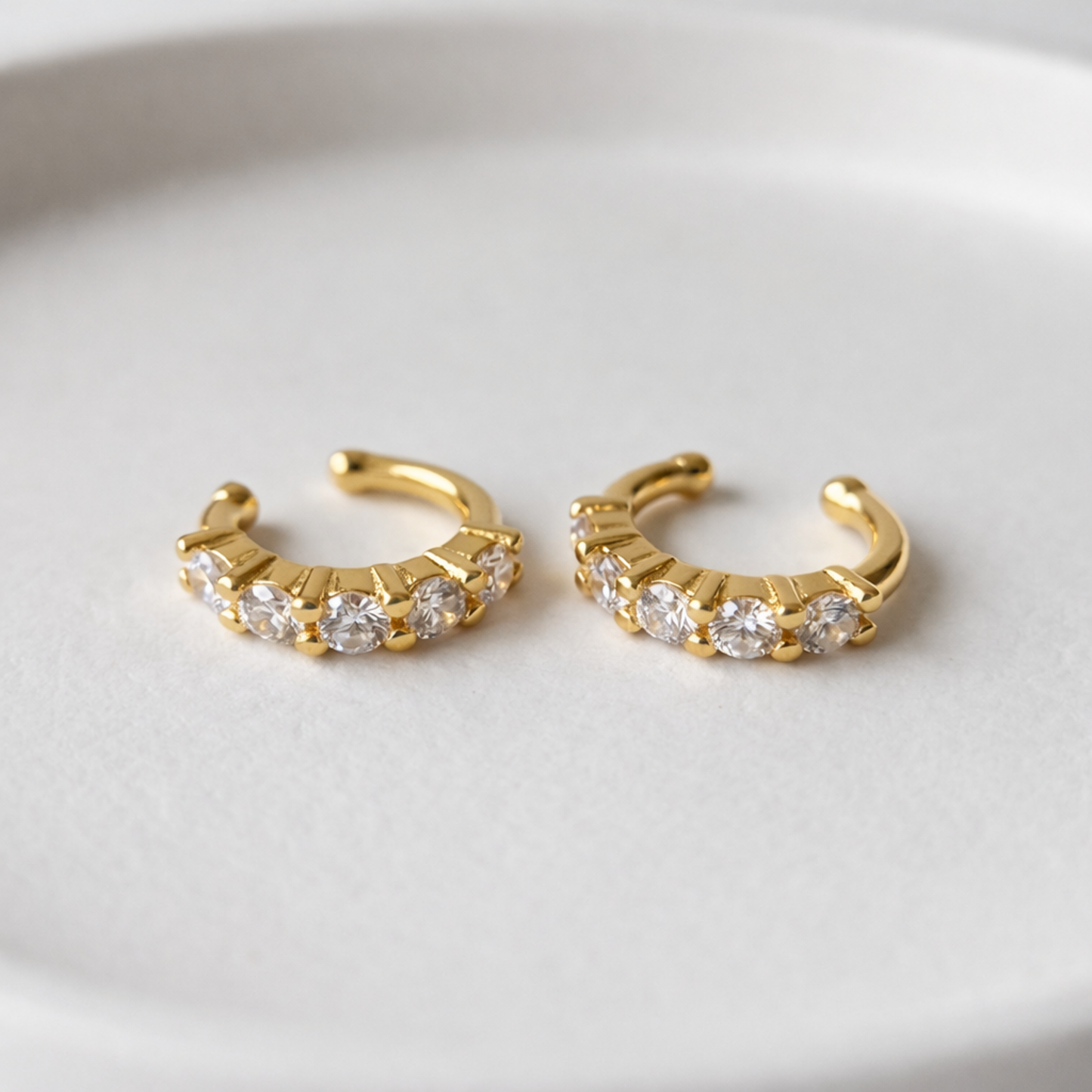 A pair of gold-plated ear cuff earrings for women featuring five brilliant prong-set stones on a white background.