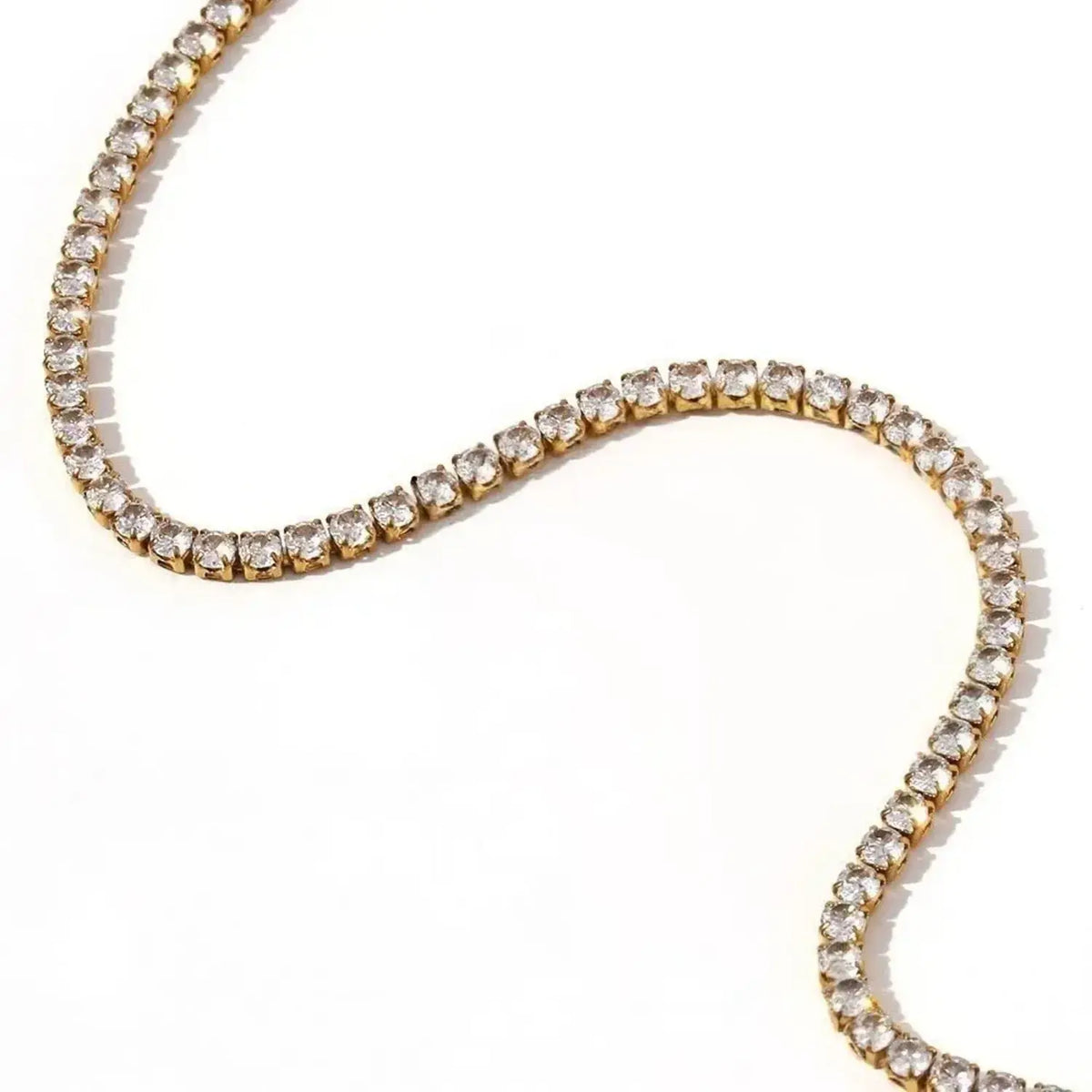 A gold tennis necklace with clear round-cut stones, arranged in a curved S-shape on a plain white background.