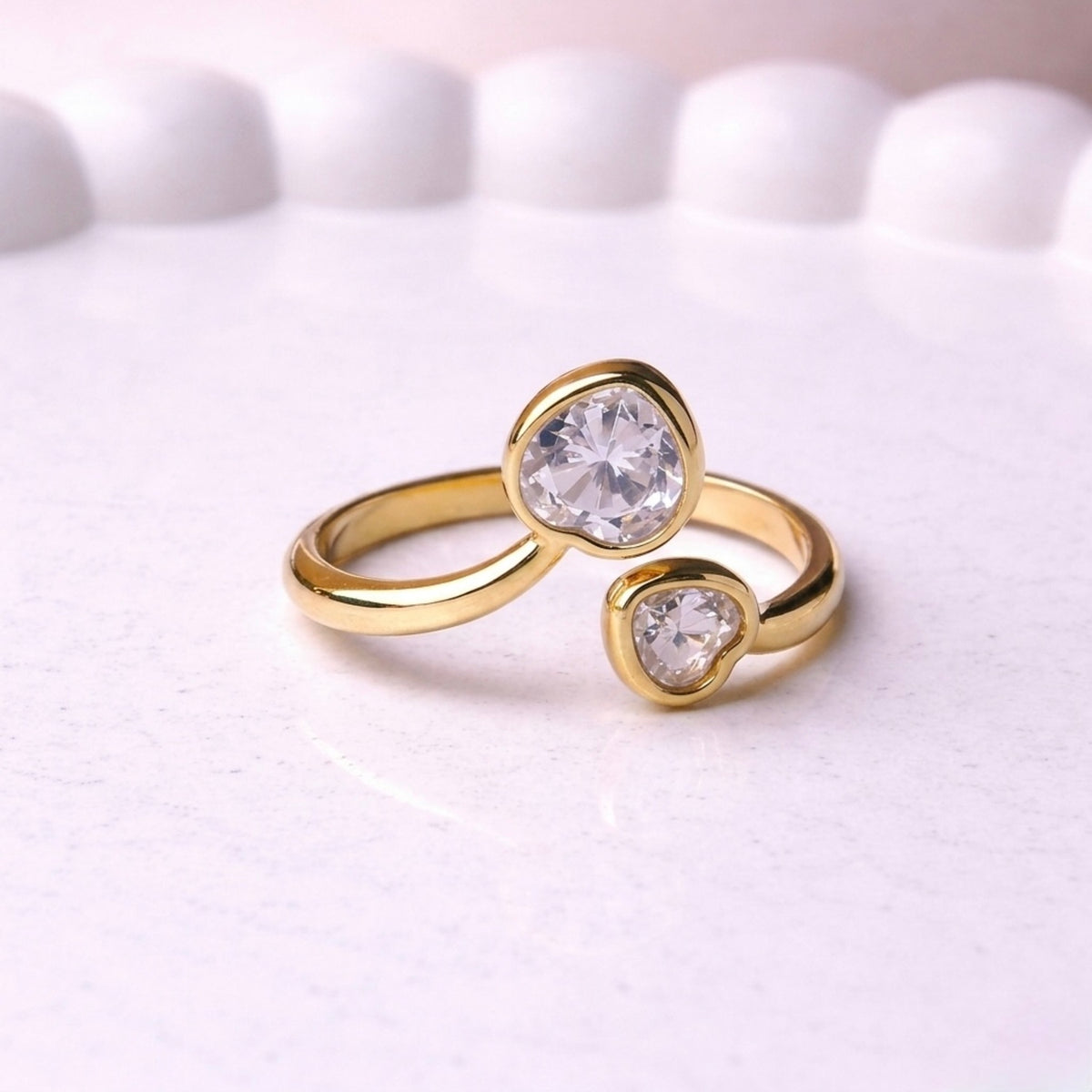 Gold plated adjustable ring for women featuring two heart-cut white stones of different sizes in a bypass wrap design, displayed on a white surface