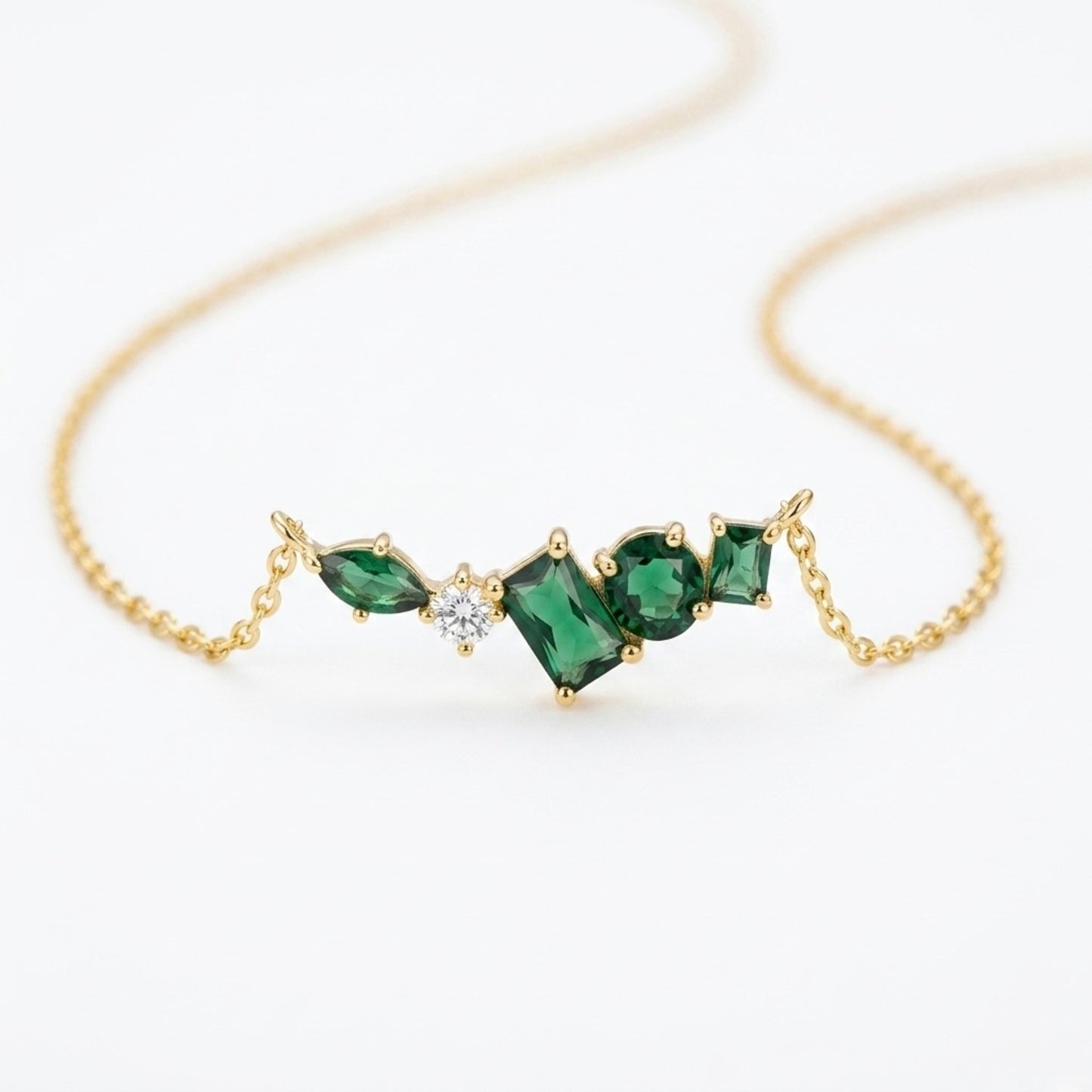 A close-view of a gold-plated stainless steel chain for women featuring an asymmetrical pendant bar set with various emerald green and white crystal stones.