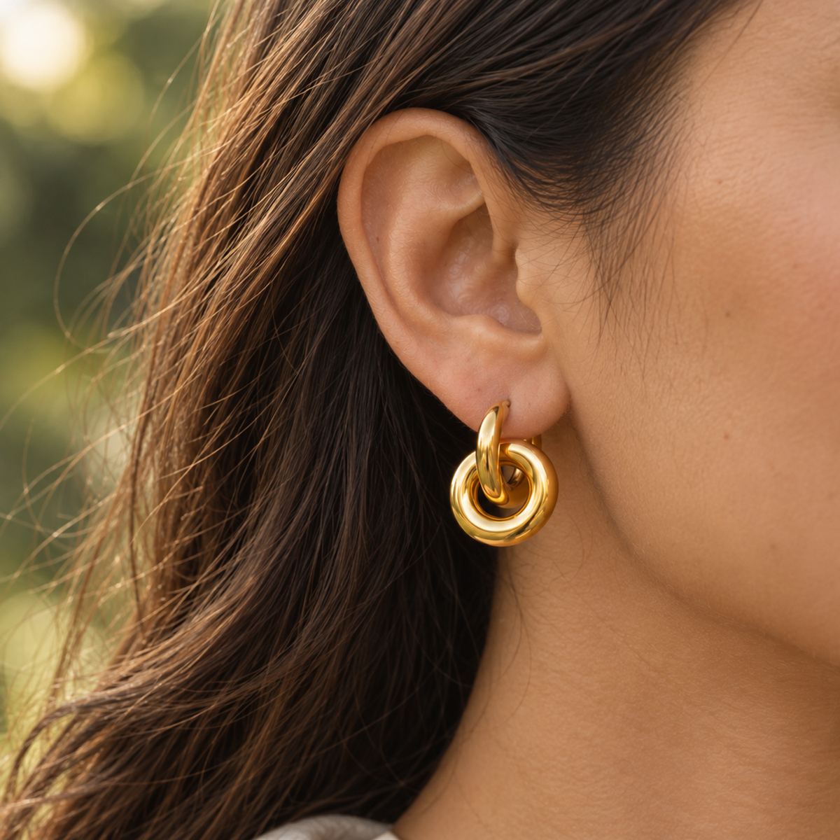 A close-up of a woman's ear wearing a polished gold huggie hoop earring with a smaller concentric hoop layered inside.