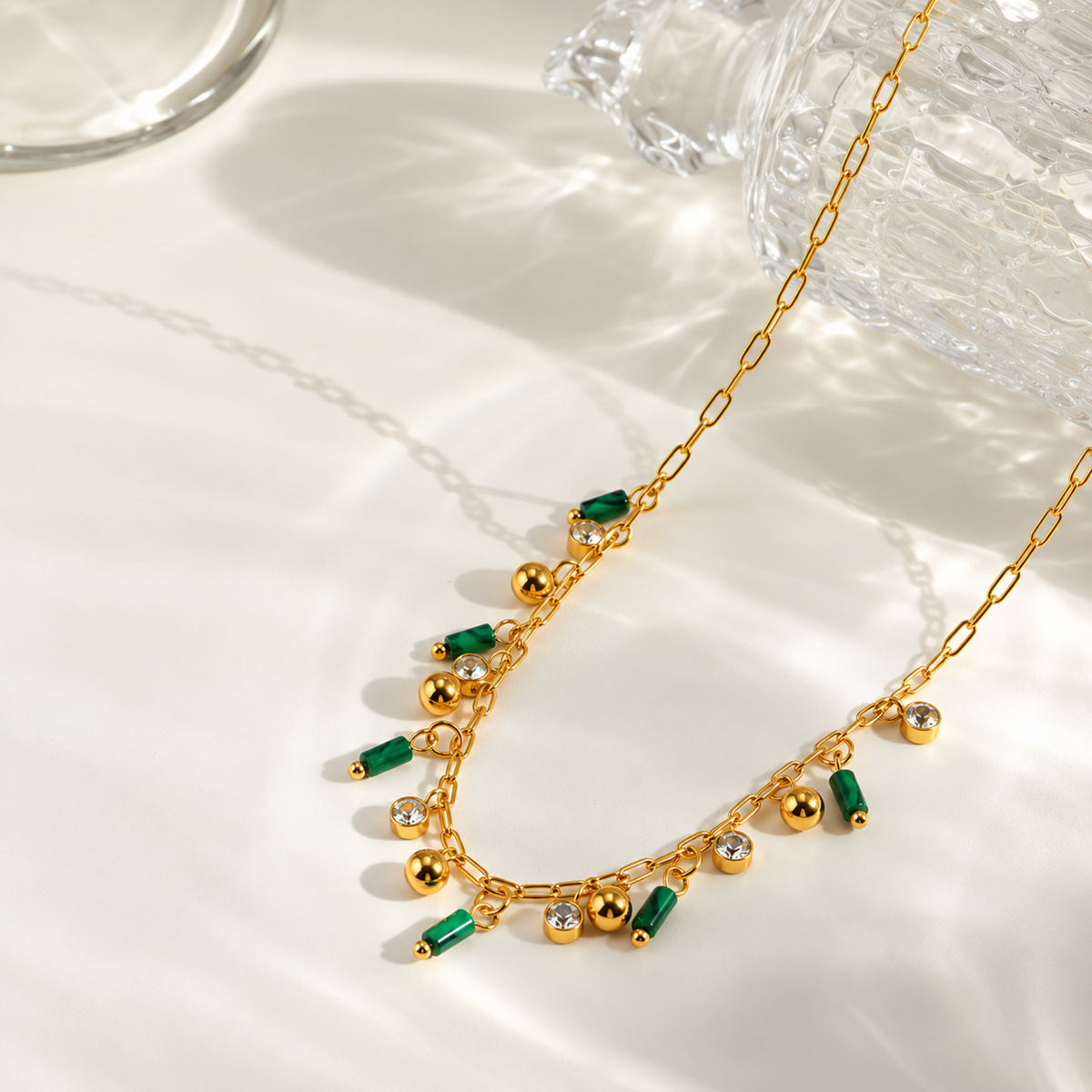 A close-view of a Green Charm Necklace with green cylindrical charms, clear crystal accents and gold-tone ball charms.