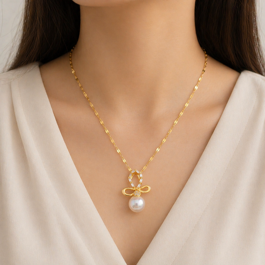 A gold-plated stainless steel chain for women featuring a crystal-encrusted bow pendant with a large white pearl drop, shown on a model