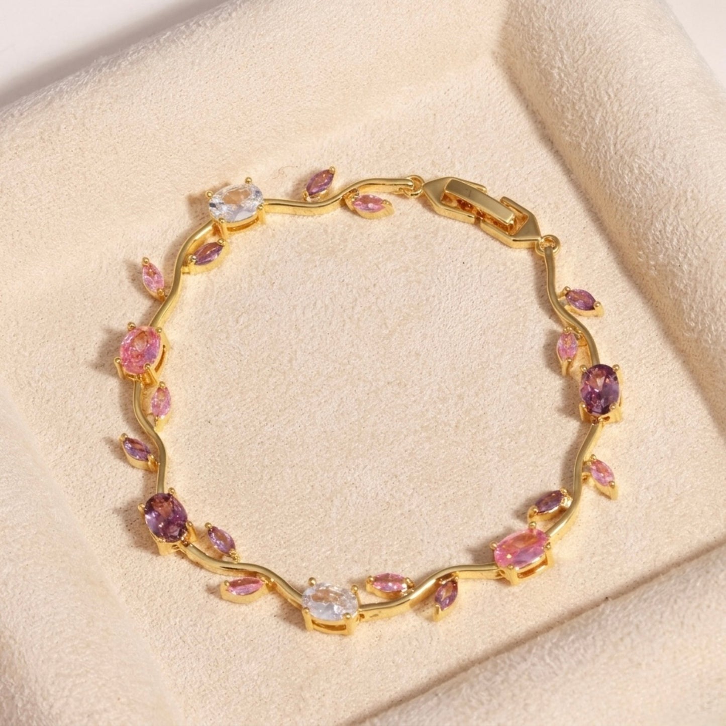 A close-view of a gold-plated floral vine chain bracelet for women featuring lavender, pink, and clear oval and marquise-cut stones, shown on a beige background