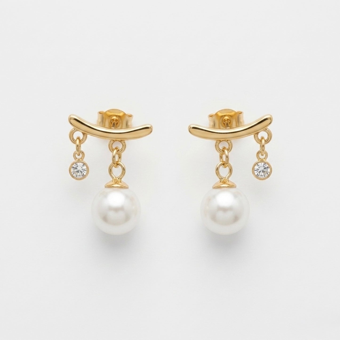 A close-view of a pair of gold-plated arc drop earrings for women featuring a central white pearl and a small clear crystal, shown on a white background