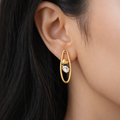 A gold-plated organic-shaped stud earrings for women featuring a small golden heart and a pear-cut crystal inside a golden loop, shown on a model