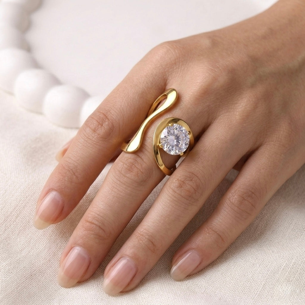 A bold and artistic gold plated adjustable statement ring for women featuring a large round white stone set in a sculptural, wavy gold-tone band on a model hand