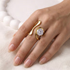 A bold and artistic gold plated adjustable statement ring for women featuring a large round white stone set in a sculptural, wavy gold-tone band on a model hand