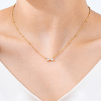 A close-view of a gold-plated stainless steel chain for women featuring small gold beads and a central crystal bow charm.
