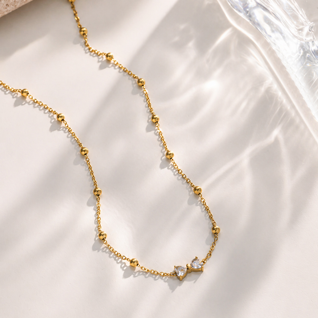 A gold-plated stainless steel chain for women featuring small gold beads and a central crystal bow charm