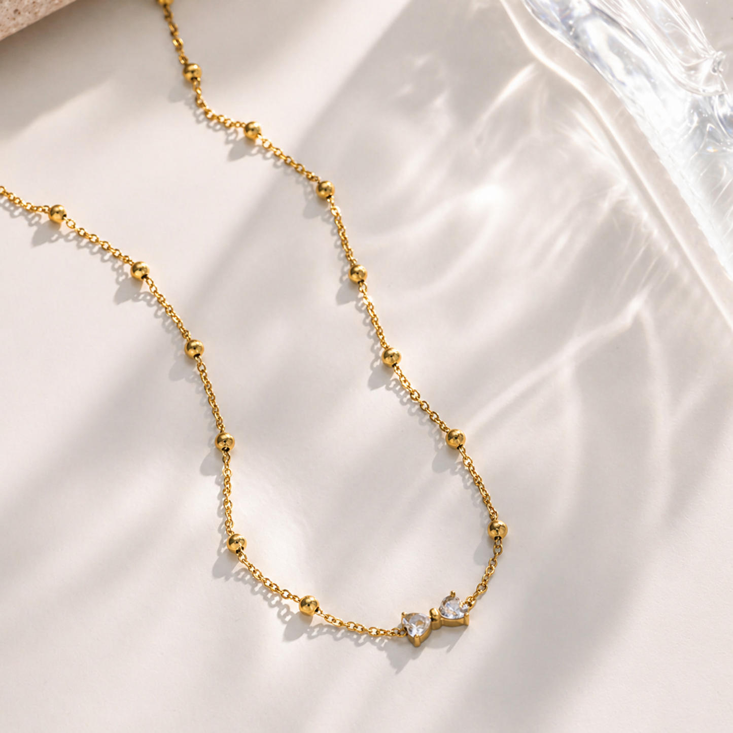A gold-plated stainless steel chain for women featuring small gold beads and a central crystal bow charm