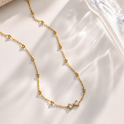 A gold-plated stainless steel chain for women featuring small gold beads and a central crystal bow charm
