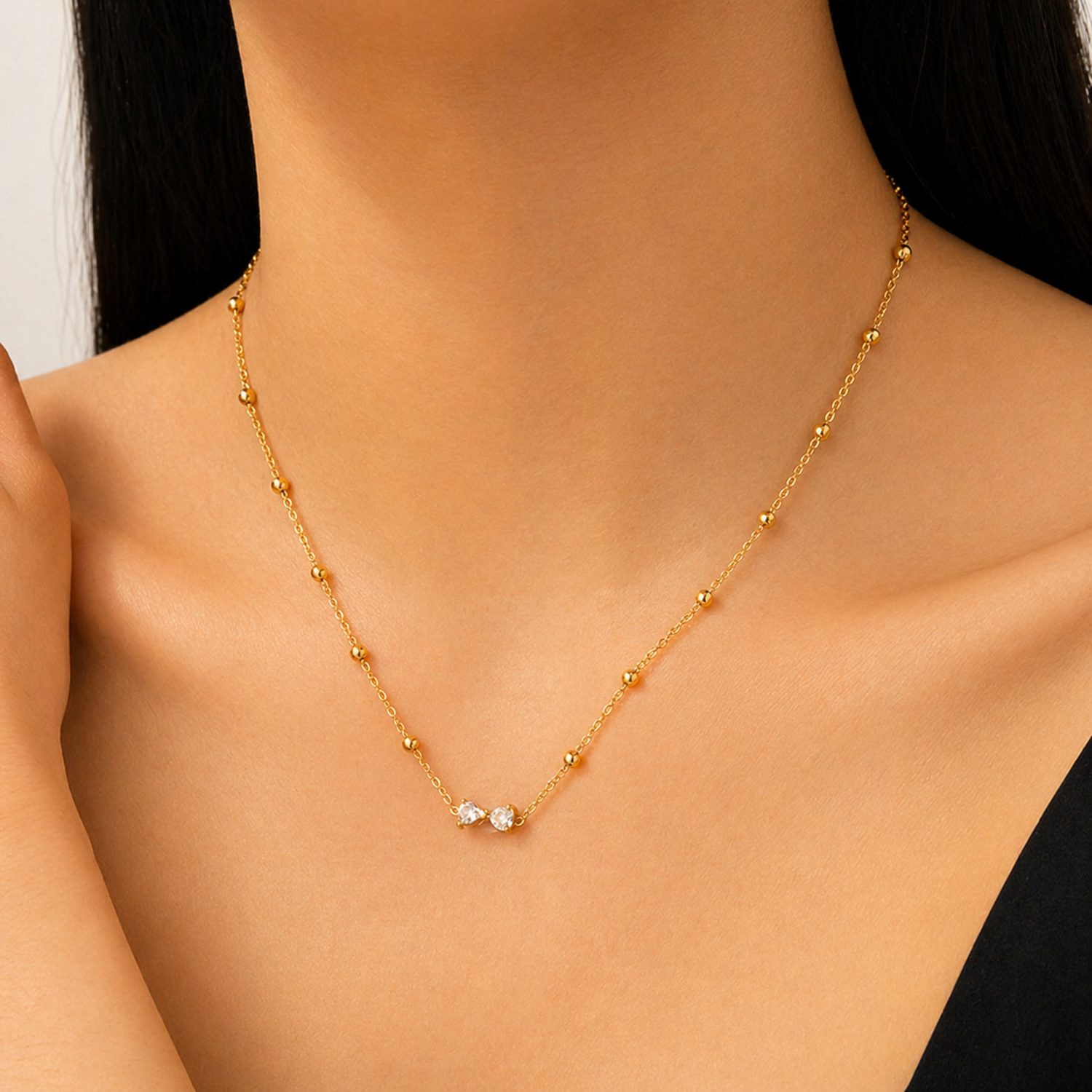 A gold-plated stainless steel chain for women featuring small gold beads and a central crystal bow charm, shown on a model