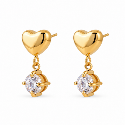 A pair of gold heart drop earrings with a polished gold heart and a clear round-cut gemstone in a prong setting, shown on a solid white background.