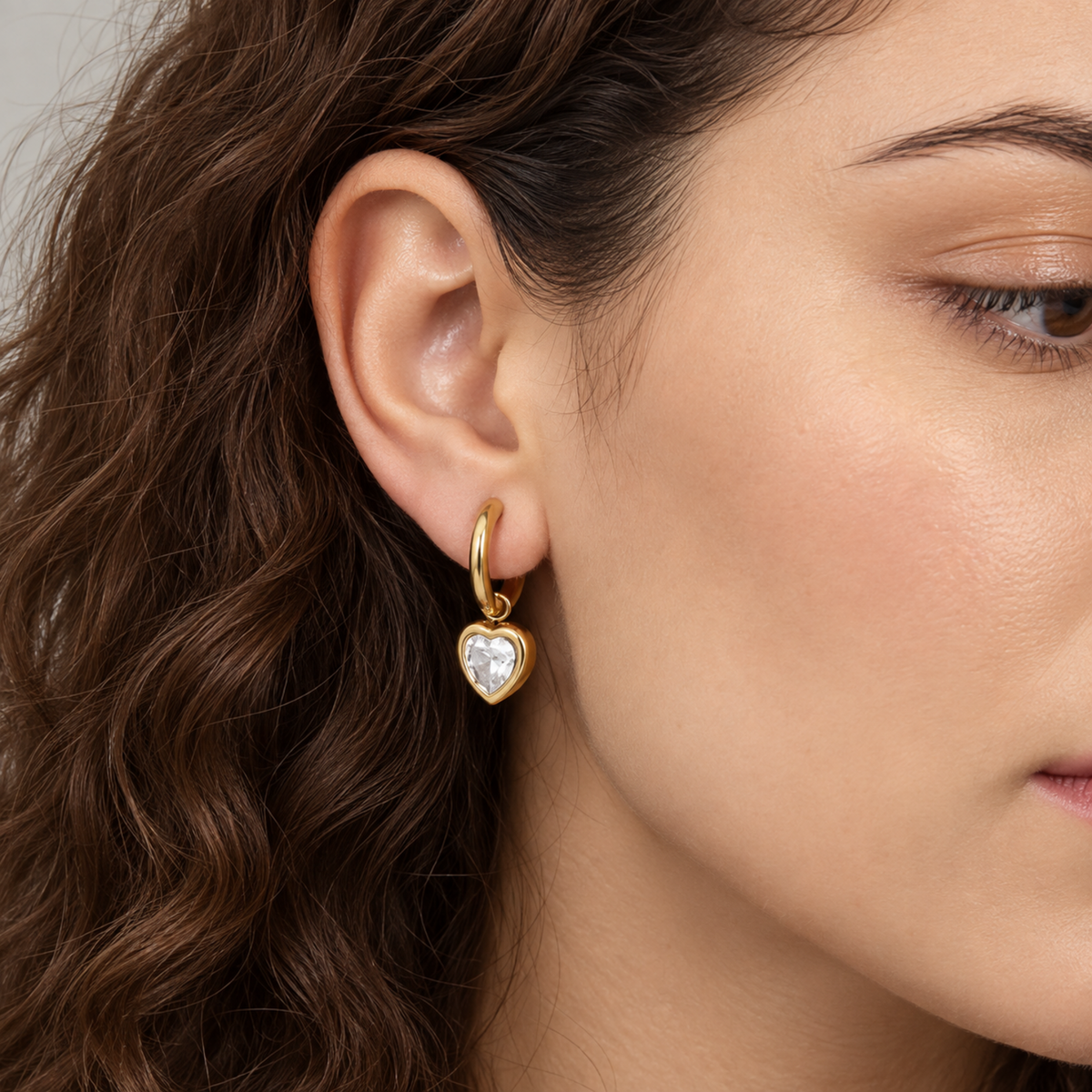 Gold heart crystal hoop earrings for women with sparkling heart-shaped drops and PVD gold plated finish on a model