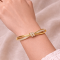 A high-end gold-plated knot bangle for women featuring a sparkling white stones central knot and a double-band cross-over design on a model hand