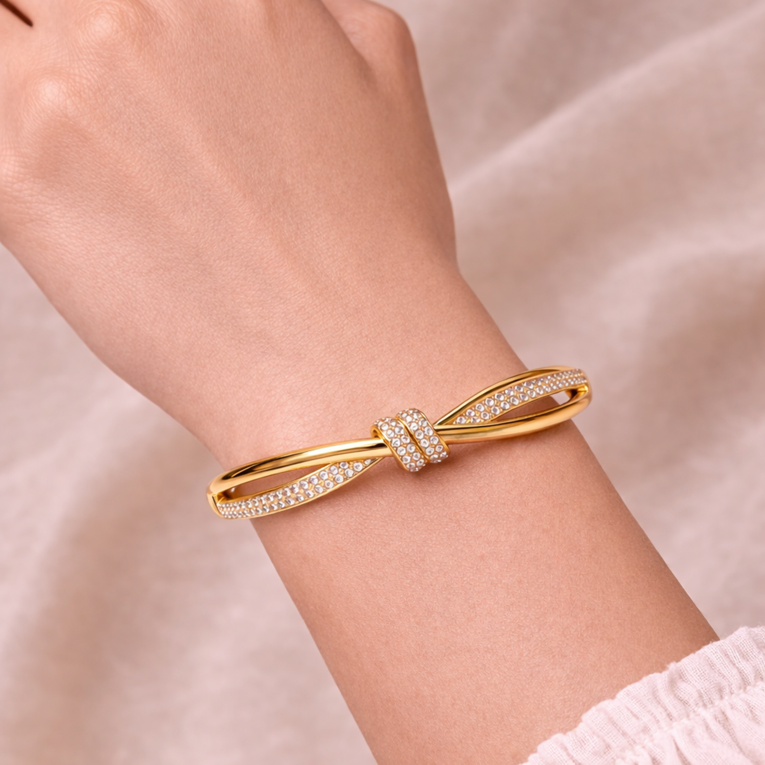 A high-end gold-plated knot bangle for women featuring a sparkling white stones central knot and a double-band cross-over design on a model hand