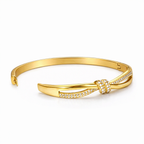 A side view of gold-plated knot bangle for women featuring a sparkling white stones central knot and a double-band cross-over design on a white background.
