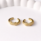 A pair of gold-plated ear cuff for women featuring one smooth polished band and one crystal-encrusted pavé band on a white ceramic tray