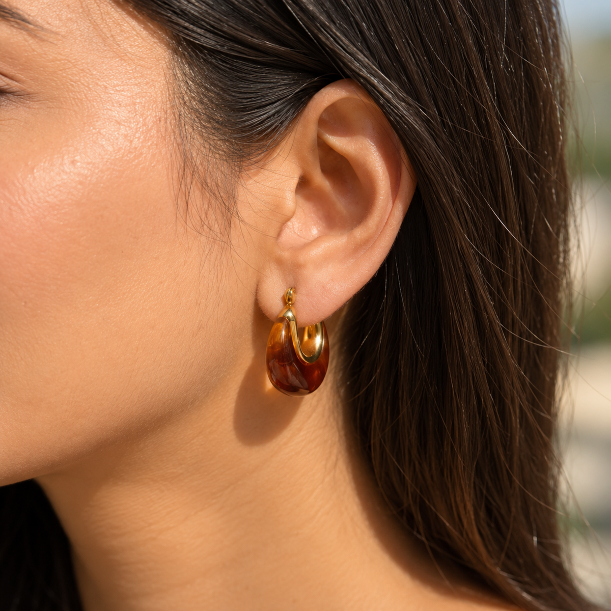 Amber resin hoop earrings for women with 18K gold plated accents, chunky rounded design and glossy finish on a model