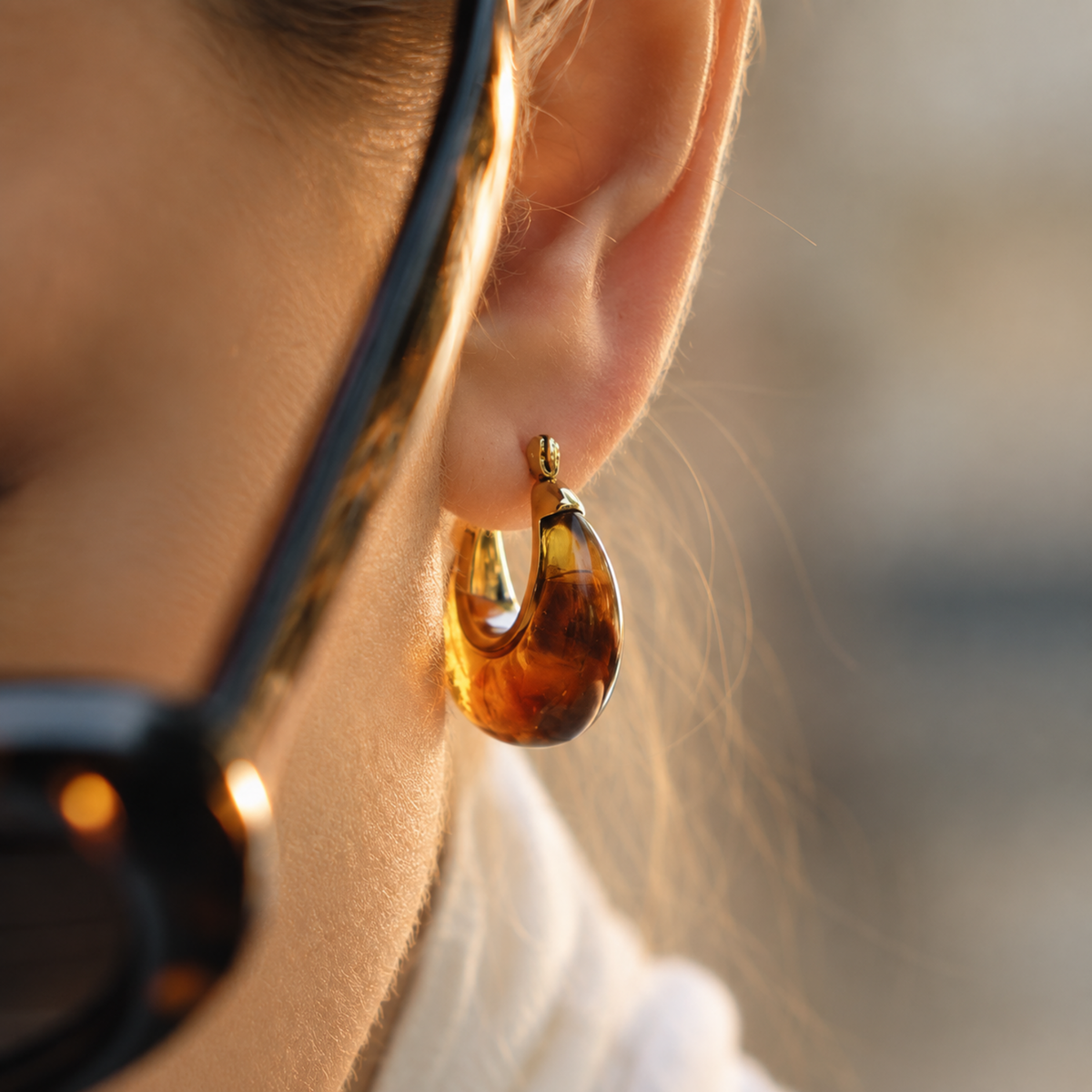 Amber resin hoop earrings for women with 18K gold plated accents, chunky rounded design and glossy finish on a model