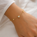 A close-view of a gold-plated ladies bracelet featuring a central crystal heart and four small polished gold heart accents on a fine chain.