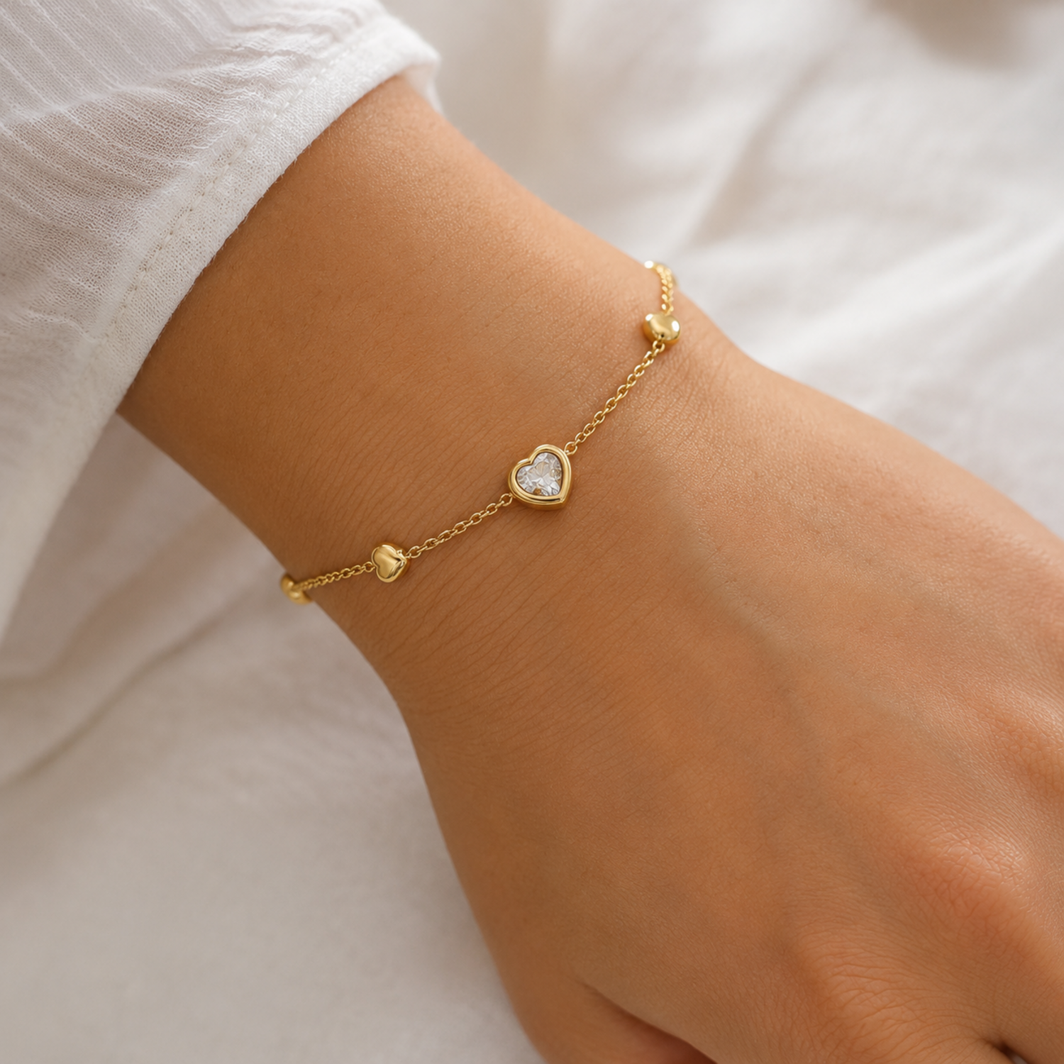 A close-view of a gold-plated ladies bracelet featuring a central crystal heart and four small polished gold heart accents on a fine chain.