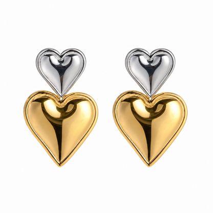 A pair of heart-shaped drop earrings, each featuring a silver plated heart on top of a larger gold plated heart, set against a plain white background.