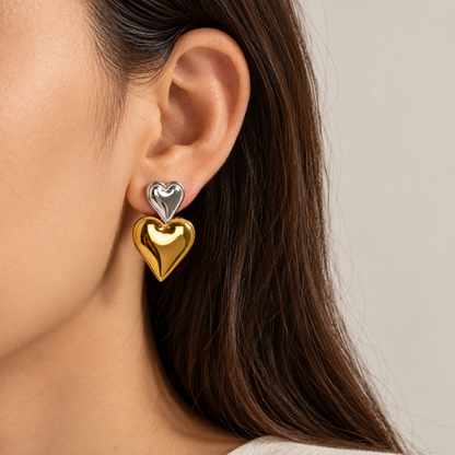 A close-up of a woman's ear wearing a double-heart stud earring with one shiny gold heart and one silver heart.