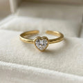A dainty gold plated adjustable ring for women featuring a single heart-cut white stone resting in a white velvet jewelry box.