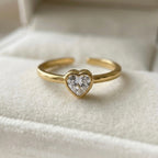 A dainty gold plated adjustable ring for women featuring a single heart-cut white stone resting in a white velvet jewelry box.