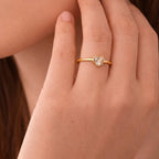 A dainty gold plated adjustable ring for women on a modeil hand featuring a single heart-cut white crystal in a bezel setting