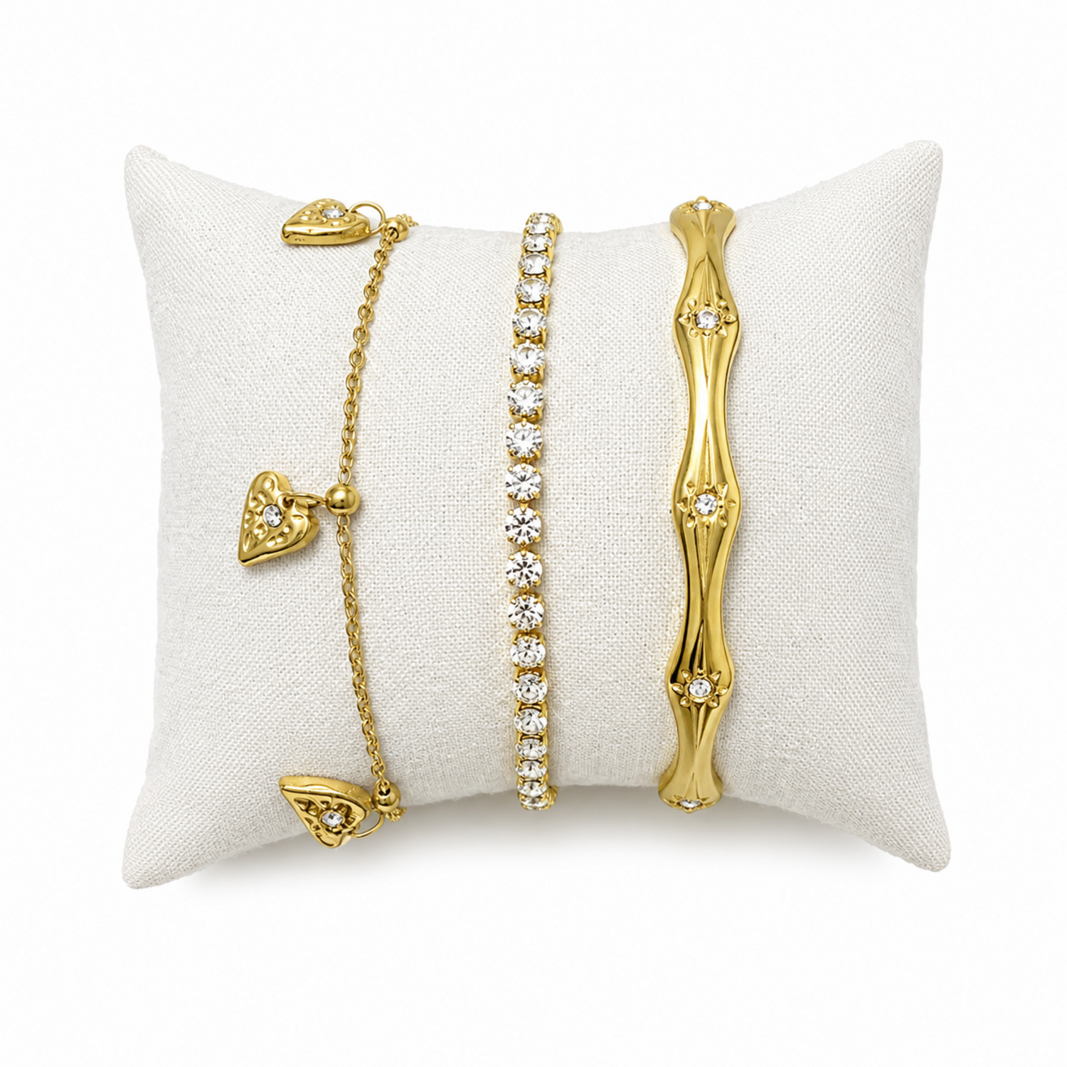A three-piece gold-plated bracelet stack for women featuring an engraved wavy starburst bangle, a classic crystal tennis bracelet, and a fine link chain with three dangling gold heart charms