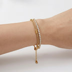 A close-view of a dual-layer gold-plated bracelet for women featuring a sparkling crystal tennis strand and a geometric box chain shown on a white background