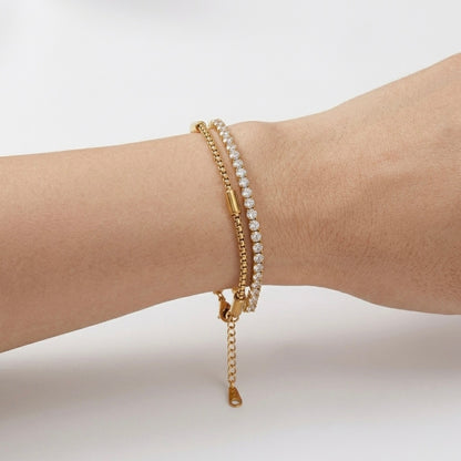 A close-view of a dual-layer gold-plated bracelet for women featuring a sparkling crystal tennis strand and a geometric box chain shown on a white background