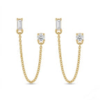 A pair of gold-plated ear chain earrings for women featuring a single baguette-cut white stone stud and a round solitaire stud connected by a fine gold chain on a white background