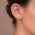 A gold-plated ear chain earrings for women featuring a single baguette-cut white stone stud and a round solitaire stud connected by a fine gold chain on a model