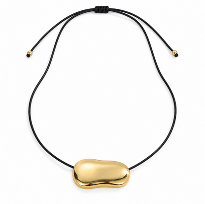 A close-view of a Gold bean pendant necklace for women with a sculptural polished pendant and black cord, minimalist modern jewellery design