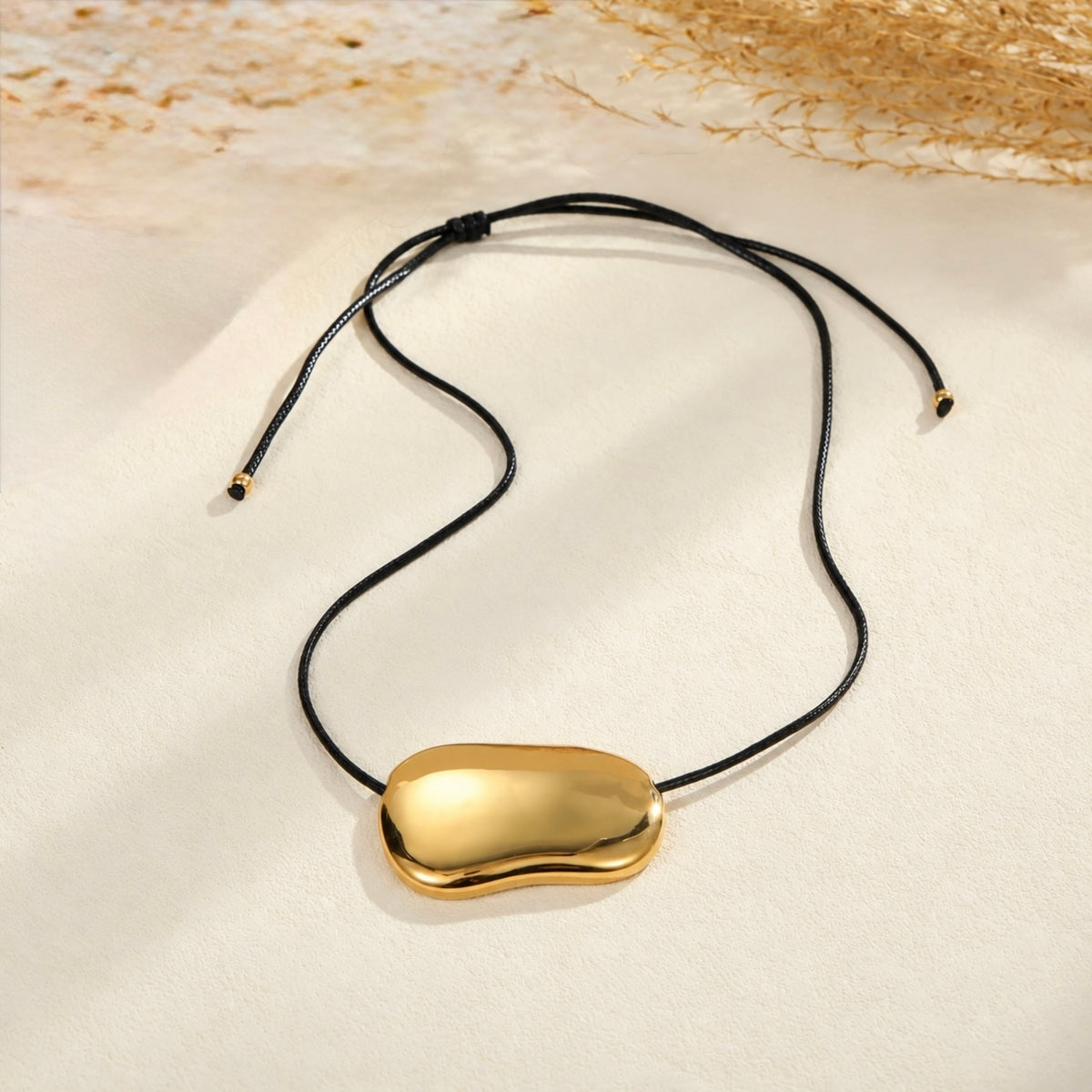 Gold bean pendant necklace for women with a sculptural polished pendant and black cord, minimalist modern jewellery design
