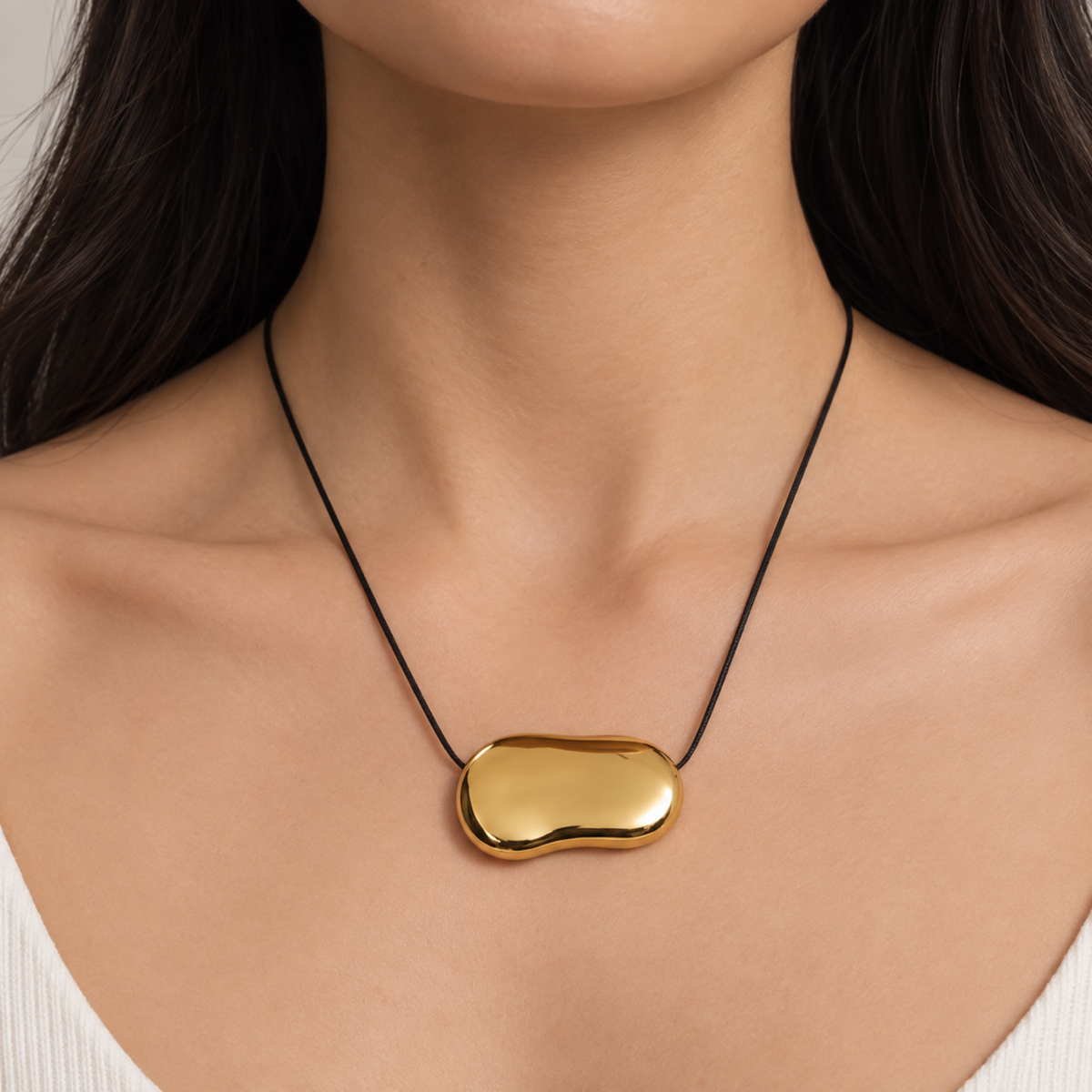 Gold bean pendant necklace for women with a sculptural polished pendant and black cord, minimalist modern jewellery design on a model