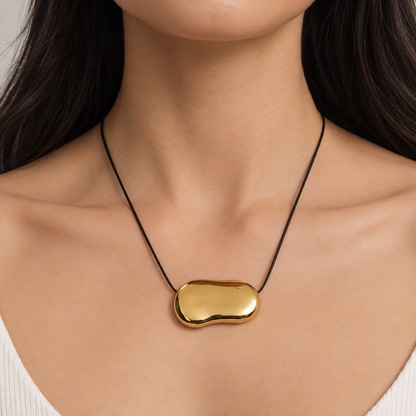 Gold bean pendant necklace for women with a sculptural polished pendant and black cord, minimalist modern jewellery design on a model