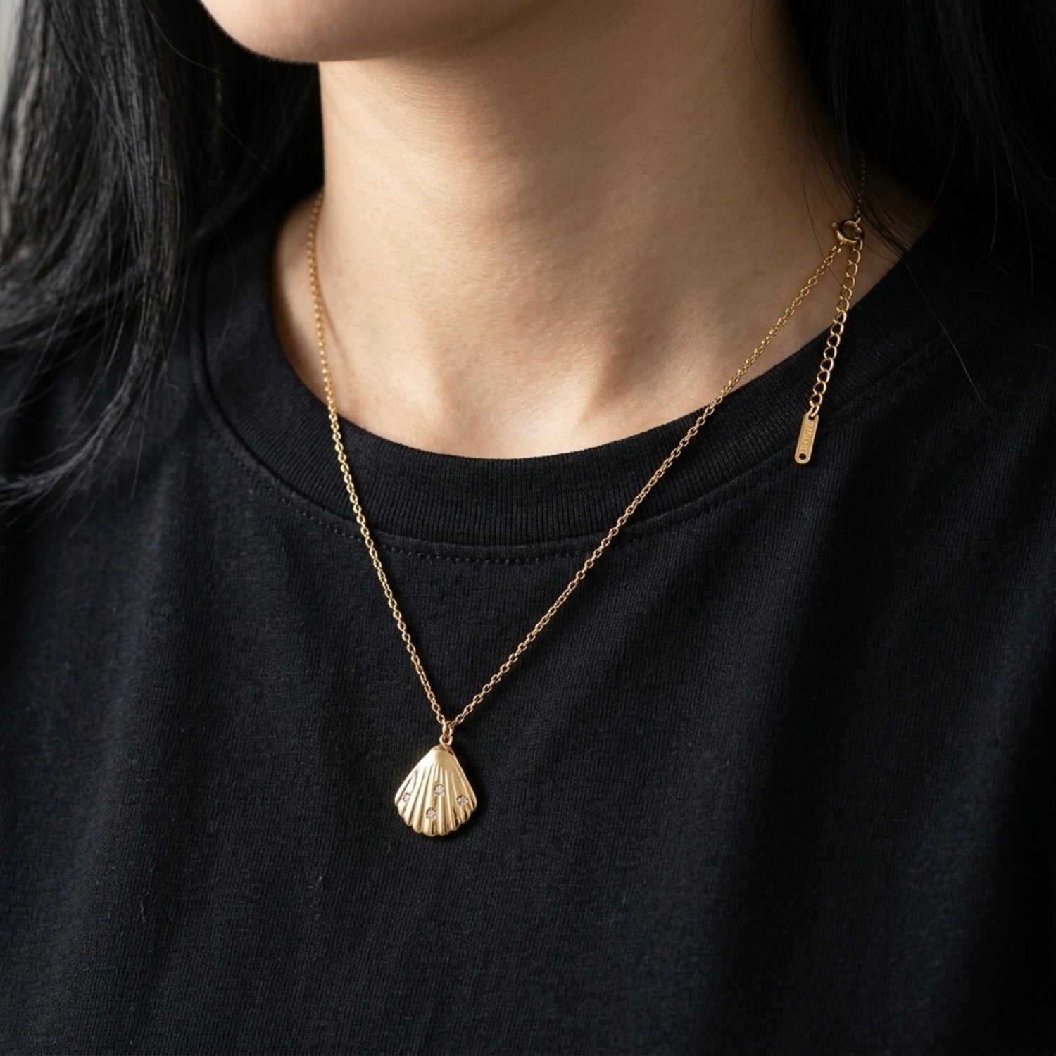 A close-view of a gold-plated stainless steel chain for women featuring a ribbed seashell pendant with four small crystals