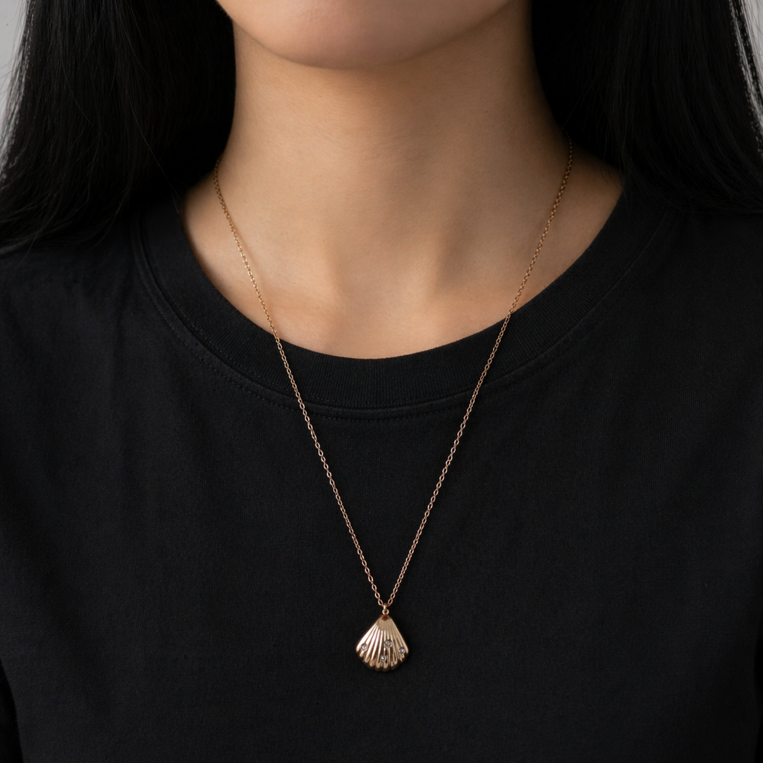 A gold-plated stainless steel chain for women featuring a ribbed seashell pendant with four small crystals on a model