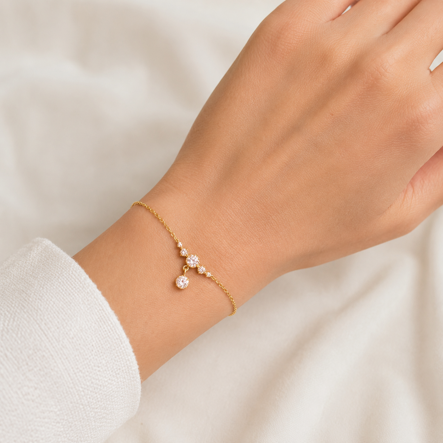 A delicate gold-plated ladies bracelet featuring a cluster of four brilliant-cut crystals and a dangling drop stone, shown on a model