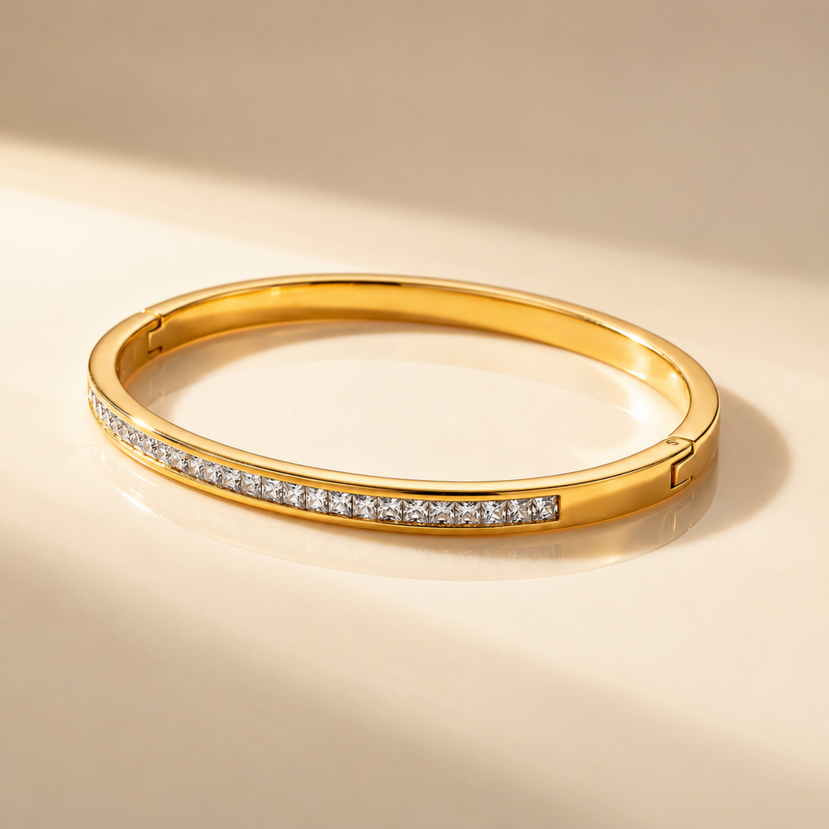 Crystal Bangle Bracelet with clear square-cut crystals set along a polished gold-plated band on a plain beige surface