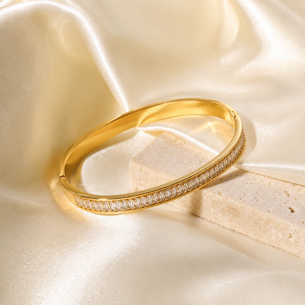 A gold-plated hinged bangle for women featuring a continuous row of channel-set baguette crystals with a secure side-clasp